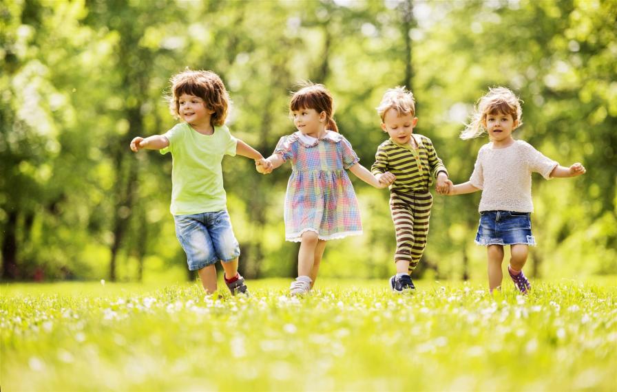 Kinder laufen Hand in Hand über die Wiese im Haus der Kinder